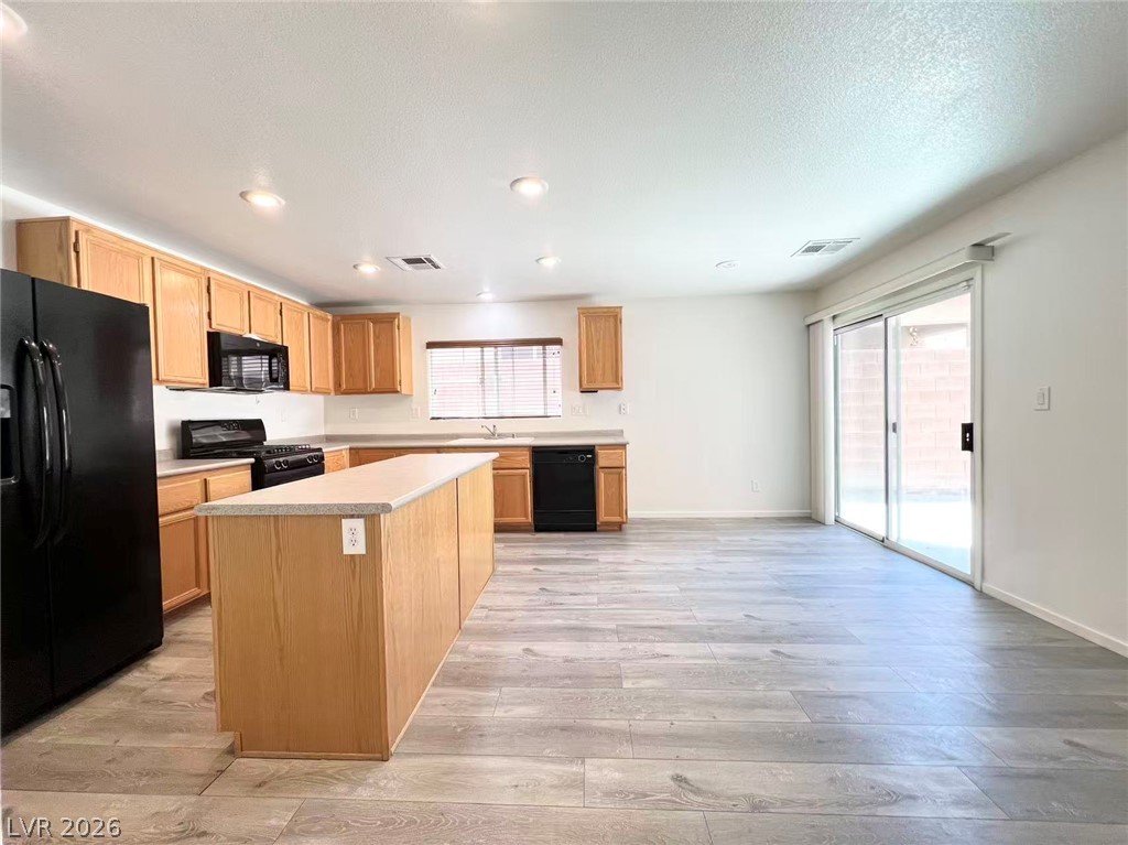 11143 Ranch Valley Street Las Vegas, NV 89179 - Photo 6 of 23 A well-lit kitchen with a central island and light wood cabinetry, offering seamless access to an outdoor area.