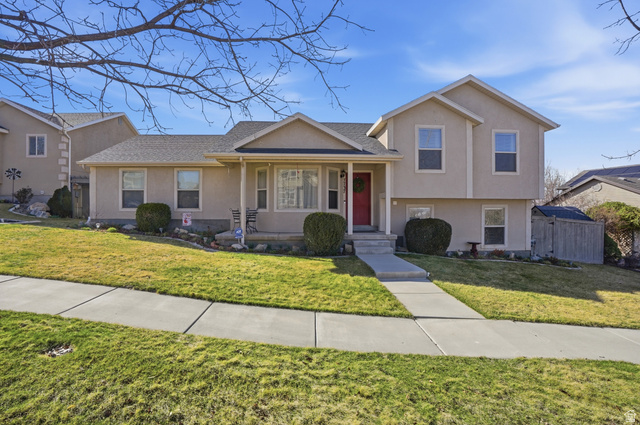 7737 Ranches Parkway Eagle Mountain, UT 84005 - Photo 1 of 28 Stucco exterior residence featuring a composite shingle roof, a prominent red entry door, a covered porch, and a concrete pathway