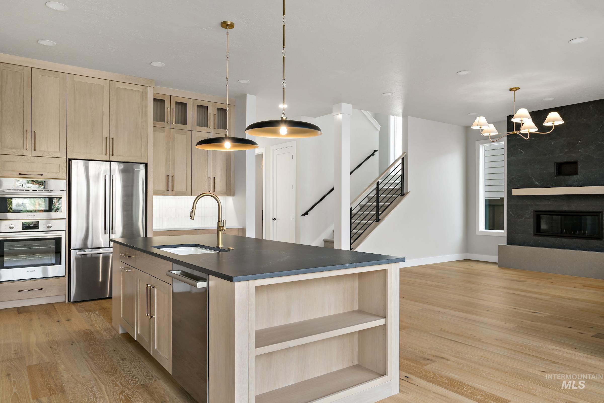 11708 North Rabbitbrush Way Boise, ID 83714 - Photo 11 of 33 Kitchen with light brown cabinetry, glass insert cabinets, a kitchen island with sink, appliances with stainless steel finishes, and light wood-style floors