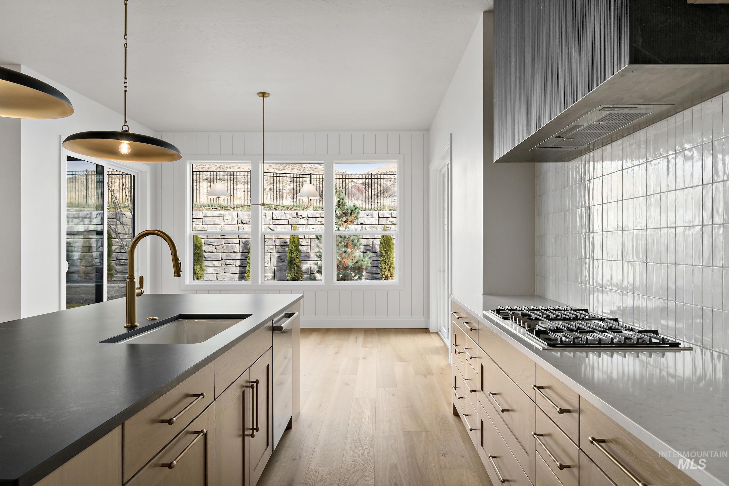 11708 North Rabbitbrush Way Boise, ID 83714 - Photo 12 of 33 Kitchen featuring light wood-style flooring, wall chimney range hood, stainless steel appliances, pendant lighting, and dark stone counters