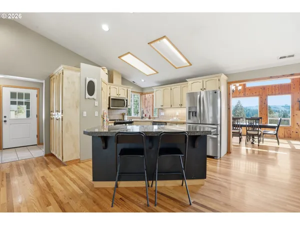 a kitchen with stainless steel appliances kitchen island granite countertop a table chairs sink and cabinets