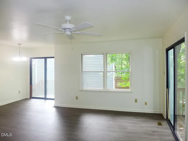 an empty room with wooden floor chandelier fan and windows