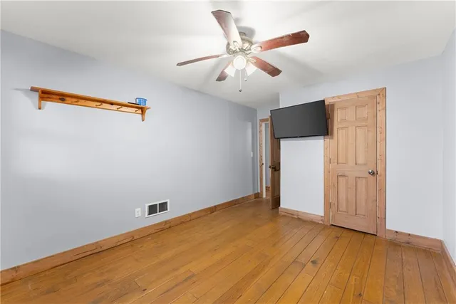 a view of an empty room with wooden floor and a chandelier fan