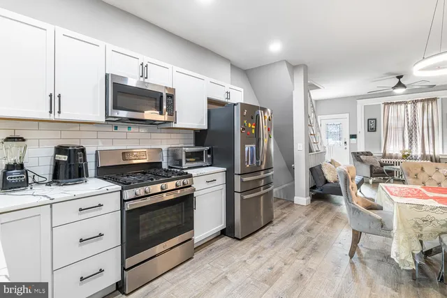 a kitchen with stainless steel appliances a stove a sink dishwasher a refrigerator microwave and white cabinets with wooden floor