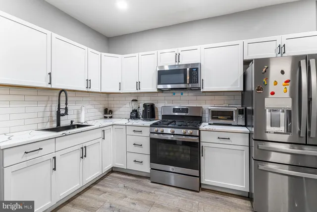 a kitchen with stainless steel appliances granite countertop white cabinets a sink a stove a refrigerator and island with wooden floor