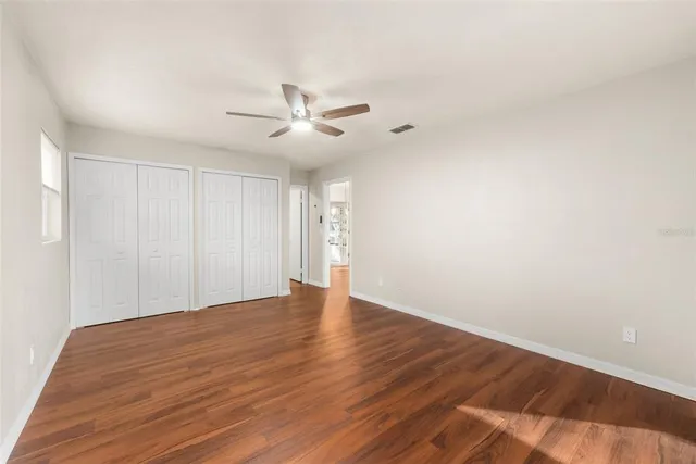a view of an empty room with wooden floor and a ceiling fan