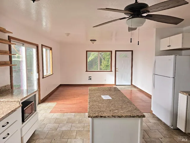 a kitchen with stainless steel appliances granite countertop a refrigerator a oven and white cabinets with wooden floor