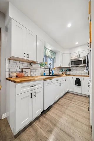 a kitchen with stainless steel appliances granite countertop a refrigerator a sink dishwasher and white cabinets with wooden floor