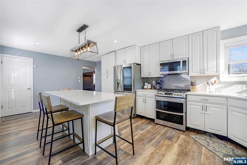 23-26 Berkshire Road Fair Lawn, NJ 07410 - Photo 17 of 36 a kitchen with stainless steel appliances a kitchen island hardwood floor sink stove dining table and chairs