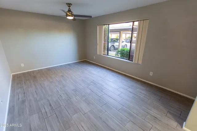 an empty room with wooden floor chandelier fan and windows
