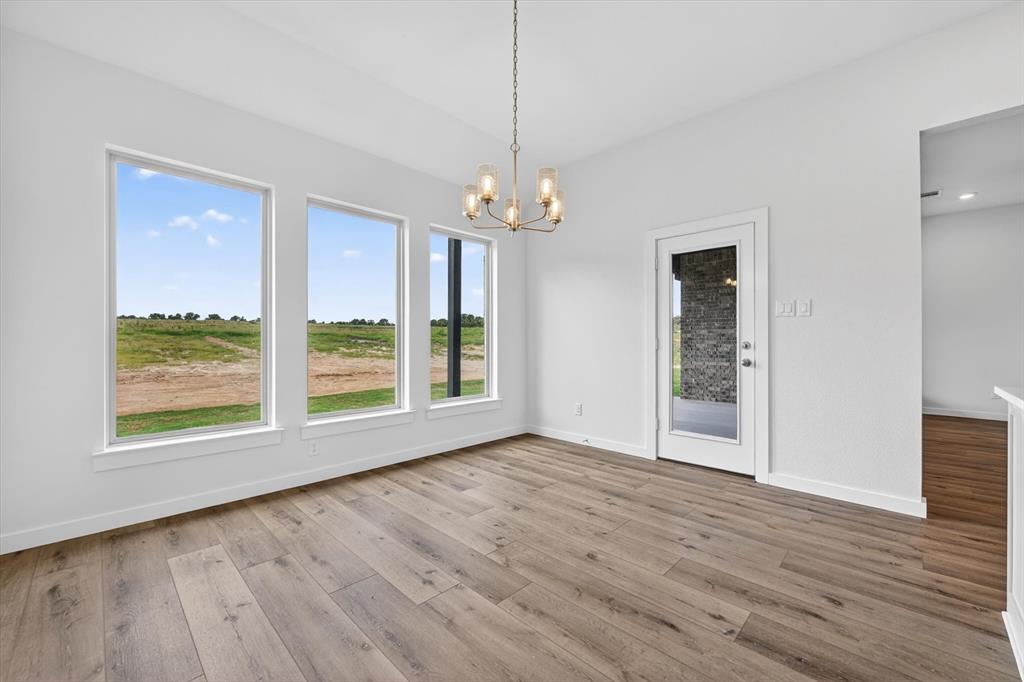 416 McAlpine Drive Springtown, TX 76082 - Photo 14 of 40 Spacious room featuring three large picture windows, wood-finish flooring, a modern chandelier with frosted glass shades, a glass-paneled door, and clean white walls