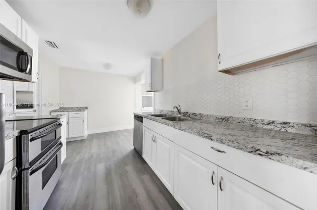 a kitchen with granite countertop a sink wooden floor and stainless steel appliances