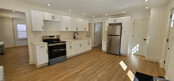 a kitchen with stainless steel appliances granite countertop a refrigerator a stove a sink and white cabinets with wooden floor