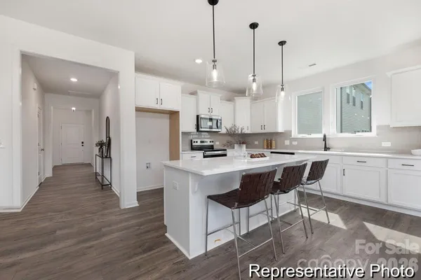 a kitchen with stainless steel appliances kitchen island granite countertop a sink a stove a refrigerator and white cabinets with wooden floor