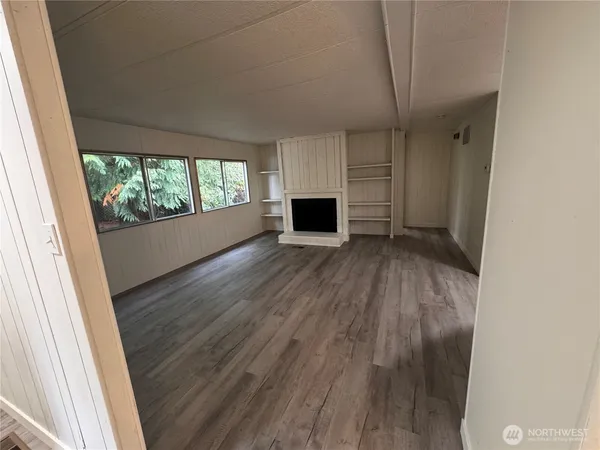 an empty room with wooden floor fireplace and windows
