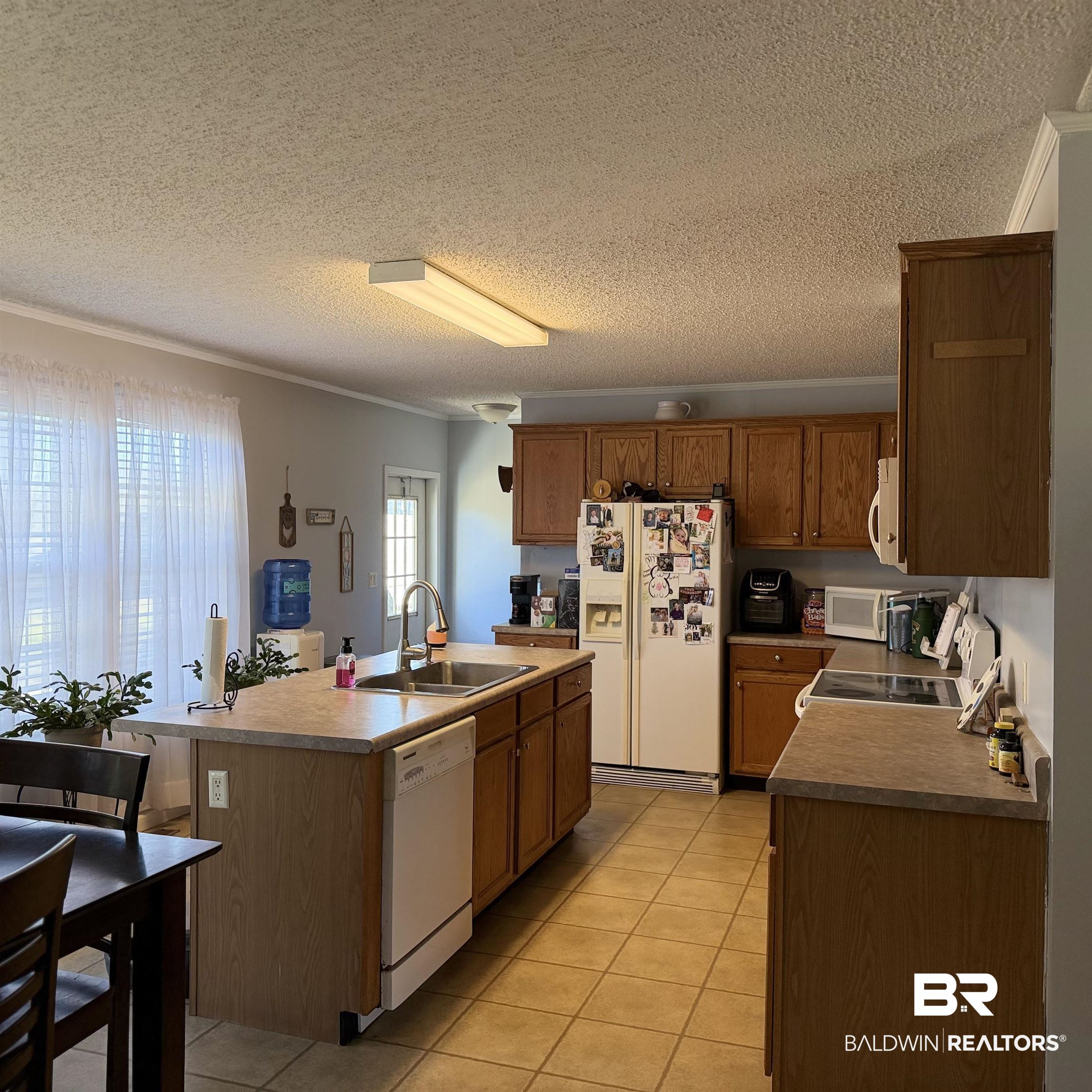447 Sugar Hill Road Monroeville, AL 36460 - Photo 6 of 27 Kitchen featuring a kitchen island with sink, white appliances, a textured ceiling, light tile patterned floors, and wood finish cabinets