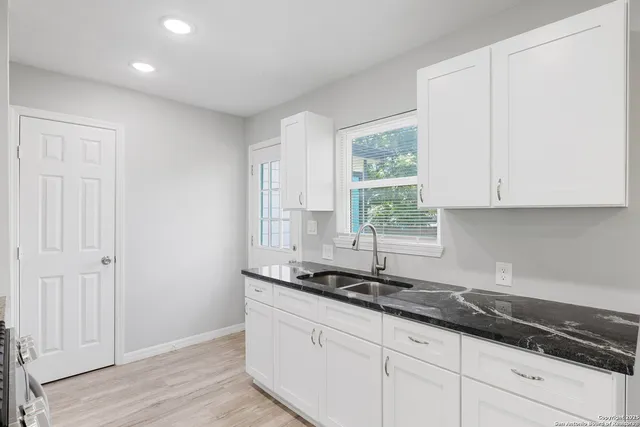 a kitchen with granite countertop white cabinets sink and window