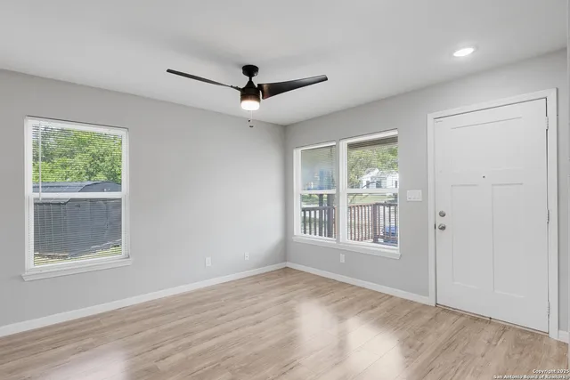 an empty room with wooden floor ceiling fan and windows