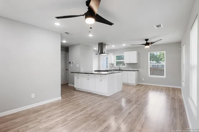 a large kitchen with a refrigerator a microwave oven a stove and white cabinets with wooden floor