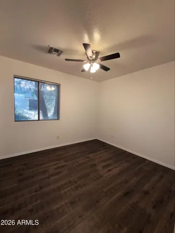 a view of an empty room with wooden floor and a ceiling fan