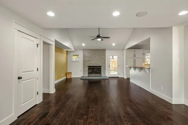 an empty room with wooden floor a ceiling fan and kitchen view