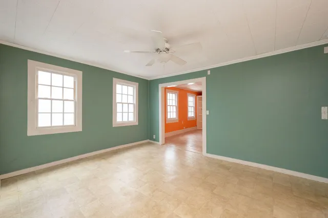 an empty room with chandelier fan and windows