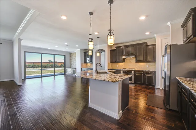 a kitchen with stainless steel appliances granite countertop wooden floors wooden cabinets a center island and a refrigerator