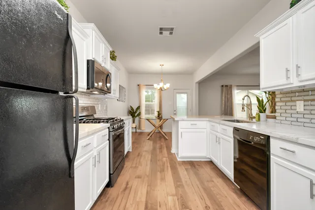 a kitchen with stainless steel appliances a stove top oven a sink a refrigerator white cabinets and wooden floor