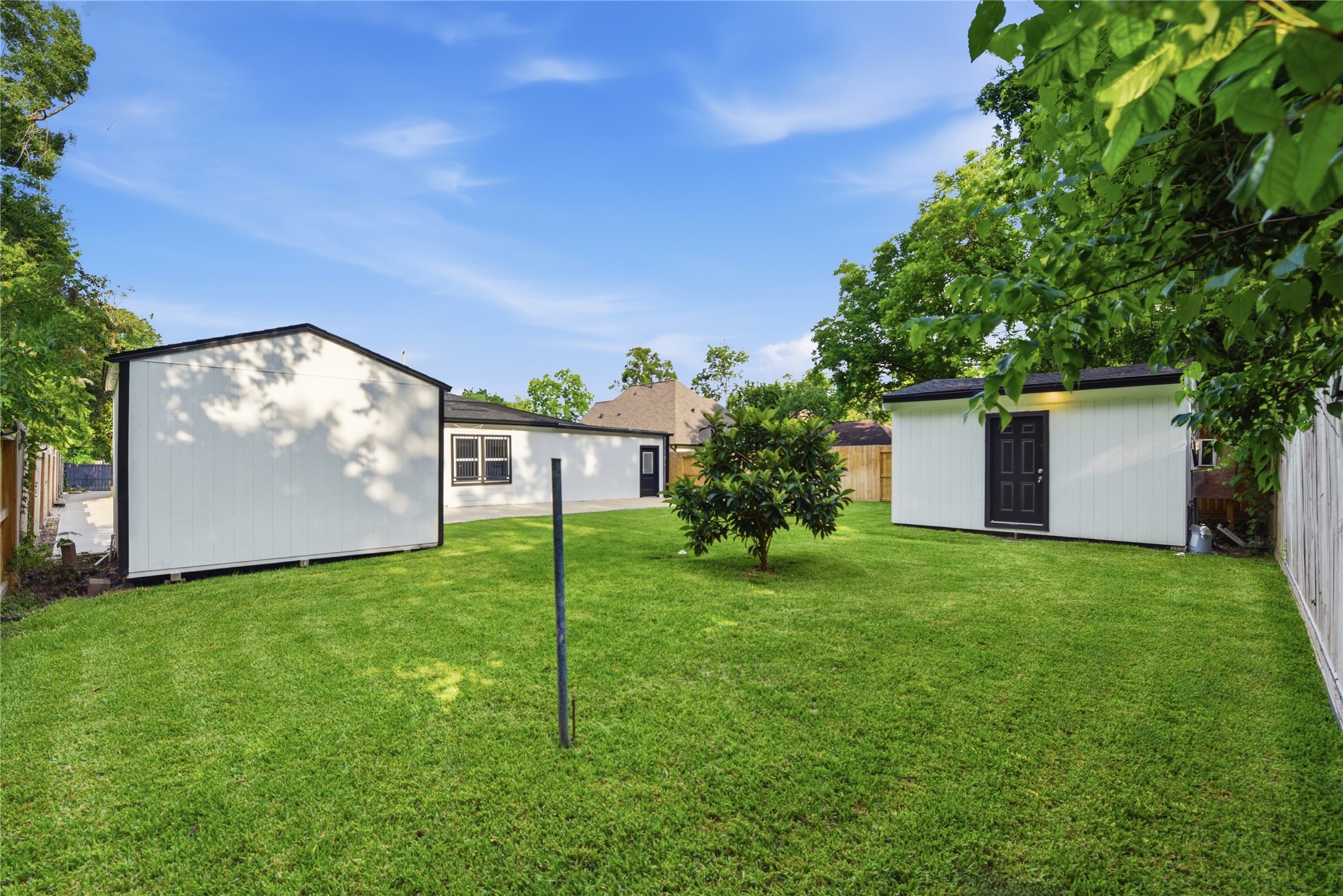 9403 Spaulding Street Houston, TX 77016 - Photo 45 of 50 Spacious backyard with well-maintained grass, featuring a small tree and two storage sheds. Ideal for outdoor activities and extra storage.