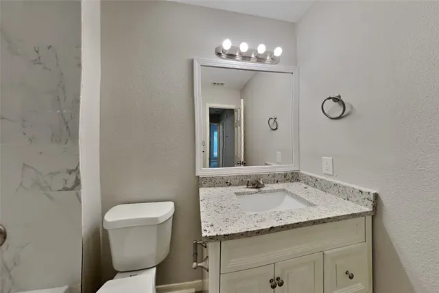 a bathroom with a granite countertop toilet a sink and a mirror