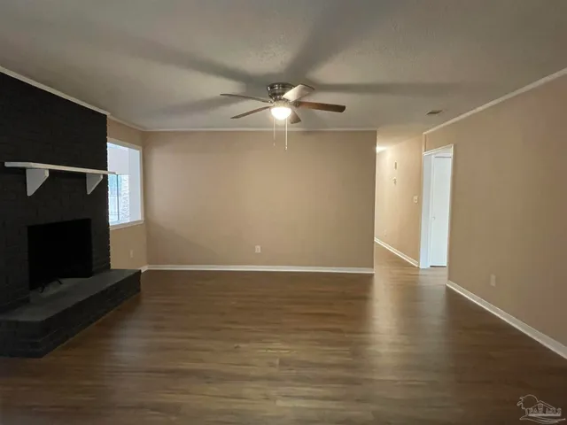 a view of an empty room with wooden floor and a fireplace