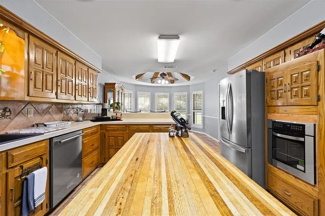 a kitchen with stainless steel appliances granite countertop a refrigerator a sink dishwasher a stove and white countertops with wooden floor