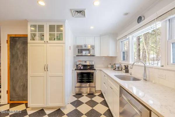 a kitchen with granite countertop a refrigerator a sink a stove and white cabinets with wooden floor