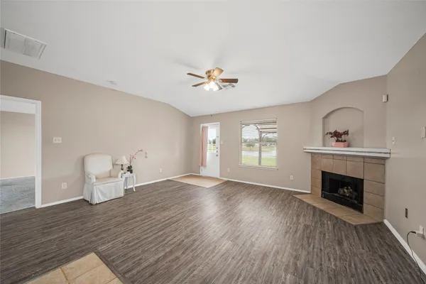 an empty room with wooden floor a fireplace a ceiling fan and windows