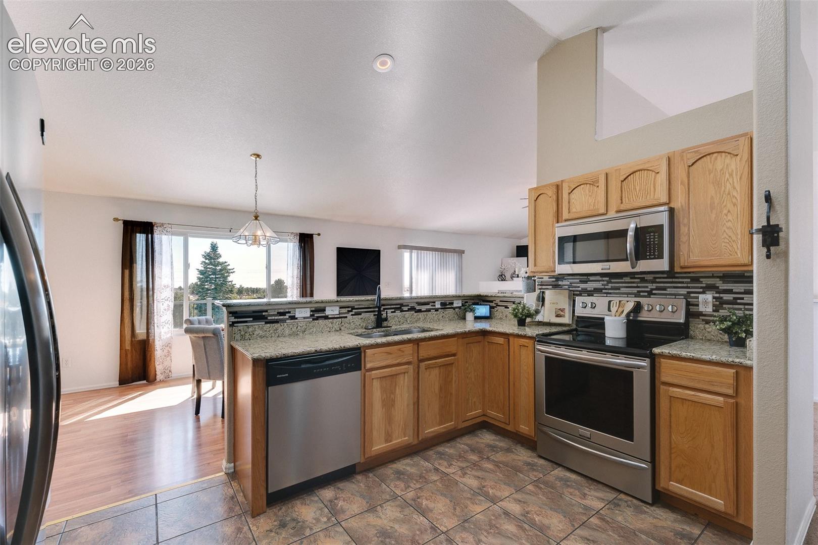 7869 Fort Smith Road Peyton, CO 80831 - Photo 19 of 50 Beautiful kitchen showcasing granite countertops, stainless steel appliances, oak cabinetry, tile flooring, and a convenient breakfast bar overlooking the main living space.