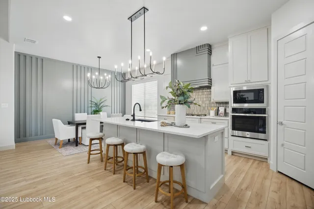 a kitchen with kitchen island stainless steel appliances a dining table chairs sink and cabinets