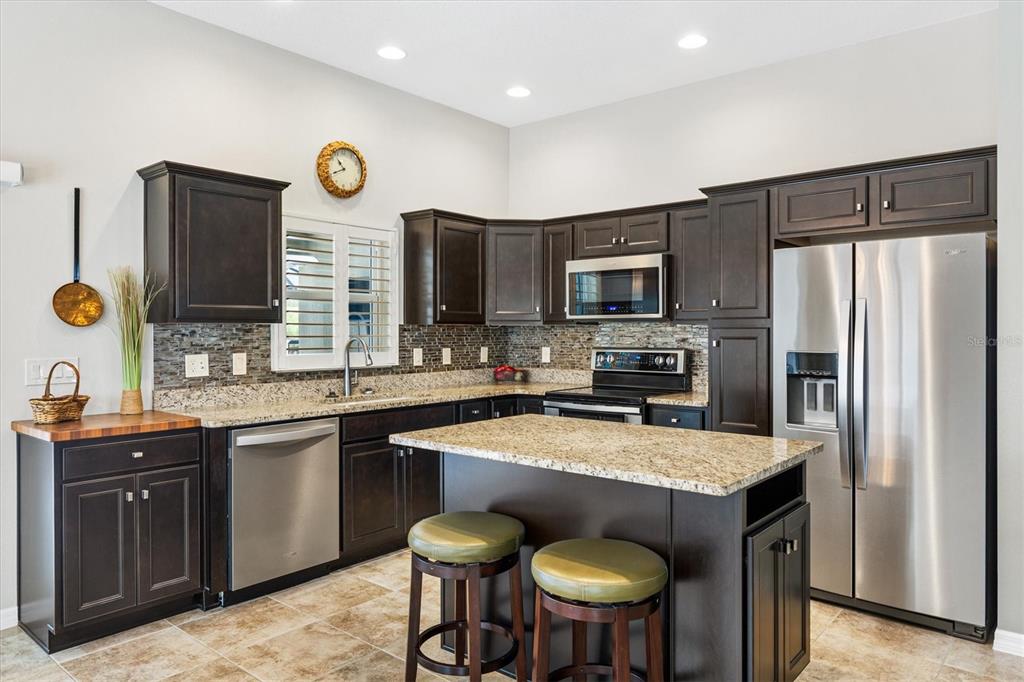 7351 Southeast 169th Cote Loop The Villages, FL 32162 - Photo 10 of 32 a kitchen with stainless steel appliances granite countertop a stove top oven a refrigerator a sink and dishwasher with wooden floor