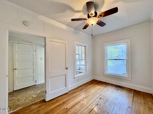 an empty room with wooden floor chandelier fan and windows