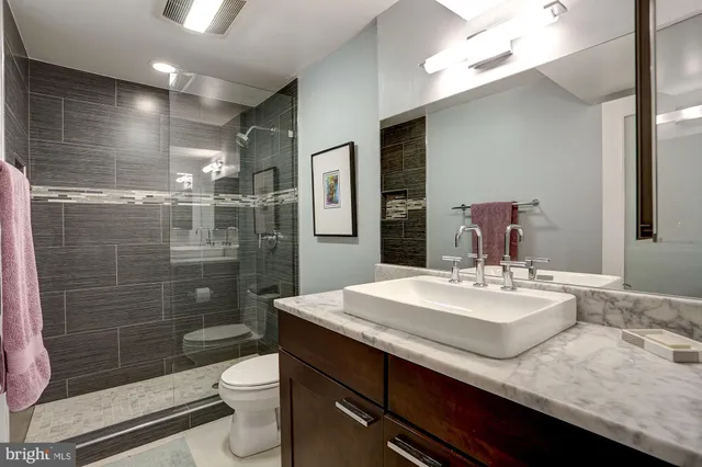 a bathroom with a granite countertop sink a toilet a mirror and shower