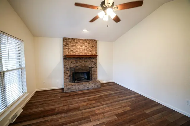an empty room with windows a fireplace a ceiling fan and wooden floor