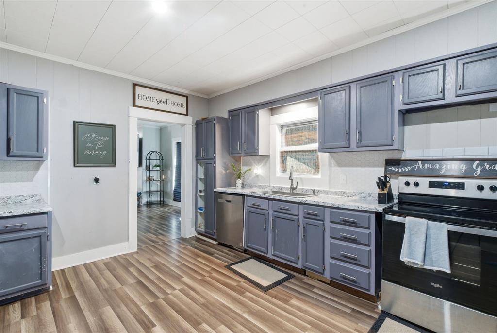 1317 4th Street Graham, TX 76450 - Photo 7 of 25 Kitchen with stainless steel appliances, ornamental molding, gray cabinets, light wood-style flooring, and light stone counters