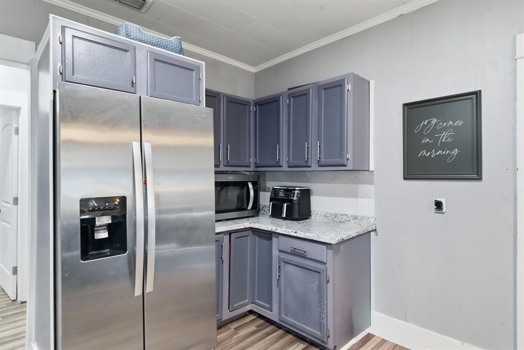 1317 4th Street Graham, TX 76450 - Photo 8 of 25 Kitchen with stainless steel appliances, ornamental molding, light wood-type flooring, gray cabinets, and light stone countertops