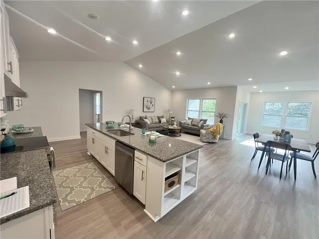 a large kitchen with stainless steel appliances a stove a sink a refrigerator and a dining table with wooden floor