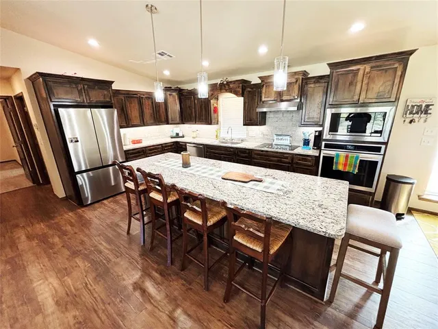 a kitchen with stainless steel appliances kitchen island granite countertop a table chairs sink and cabinets