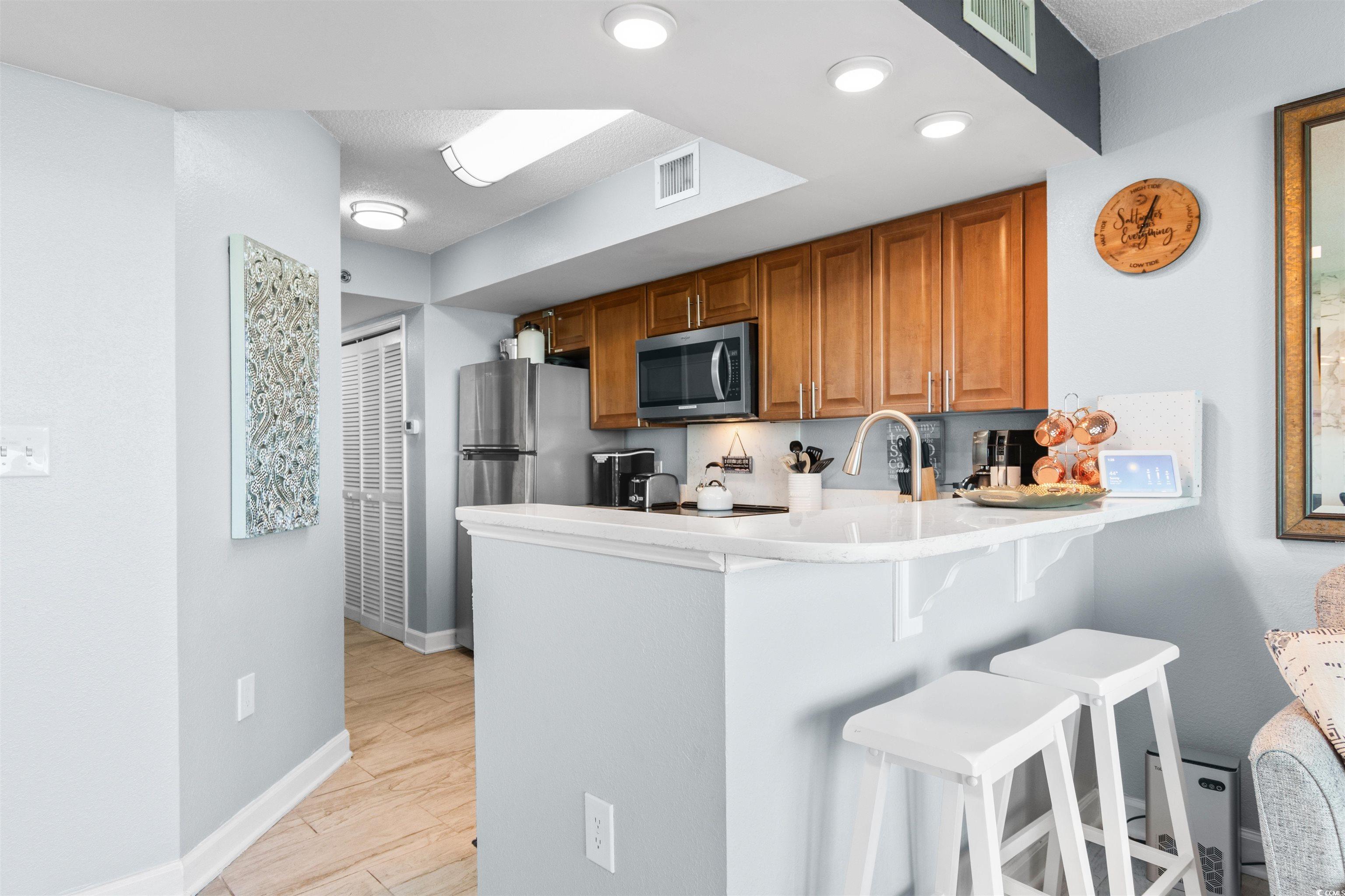 215 77th Avenue North, Unit 603 Myrtle Beach, SC 29572 - Photo 12 of 37 Kitchen with brown cabinetry, a breakfast bar, a peninsula, light wood-style floors, and stainless steel appliances