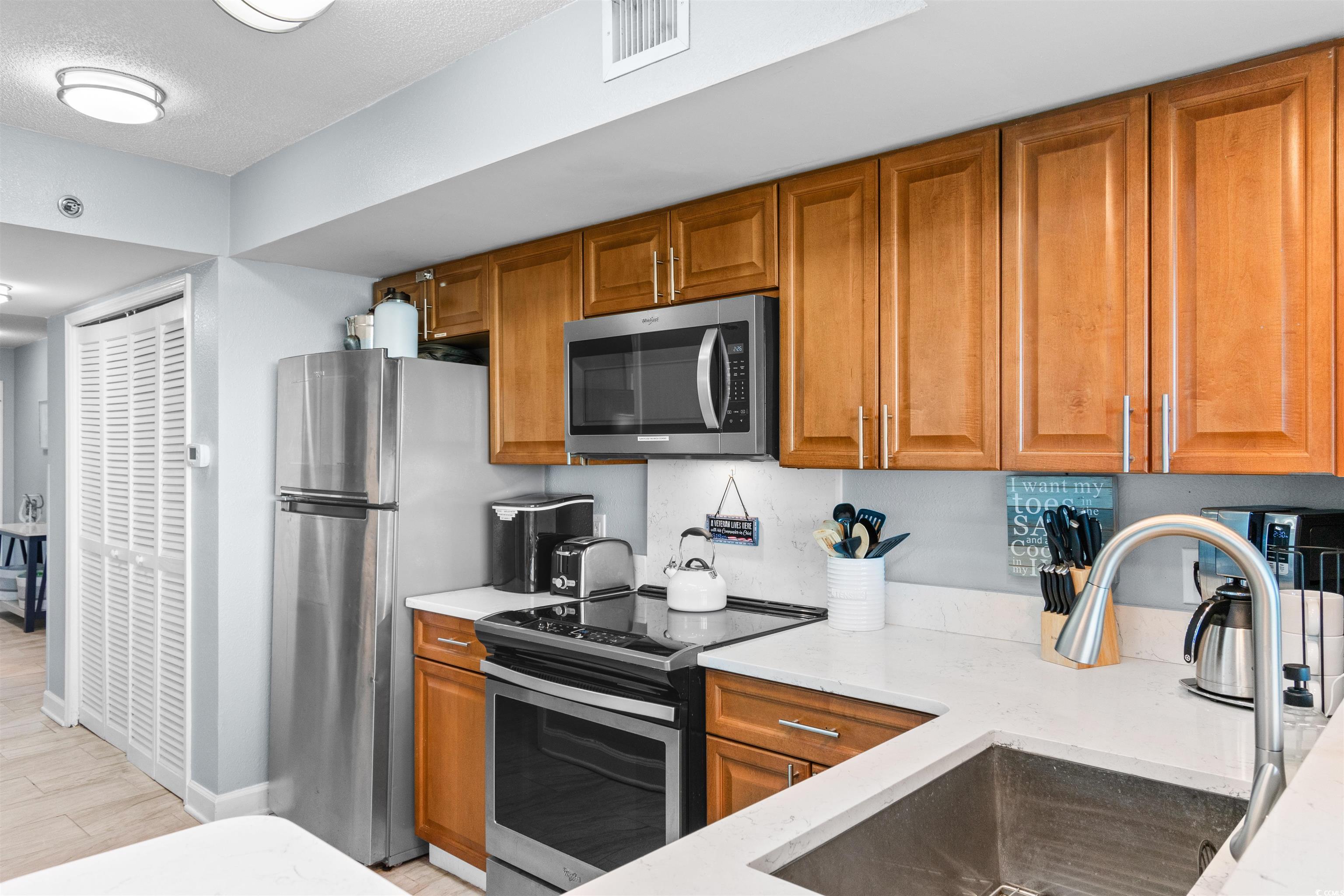 215 77th Avenue North, Unit 603 Myrtle Beach, SC 29572 - Photo 13 of 37 Kitchen with appliances with stainless steel finishes, brown cabinetry, light stone counters, and light wood-style floors
