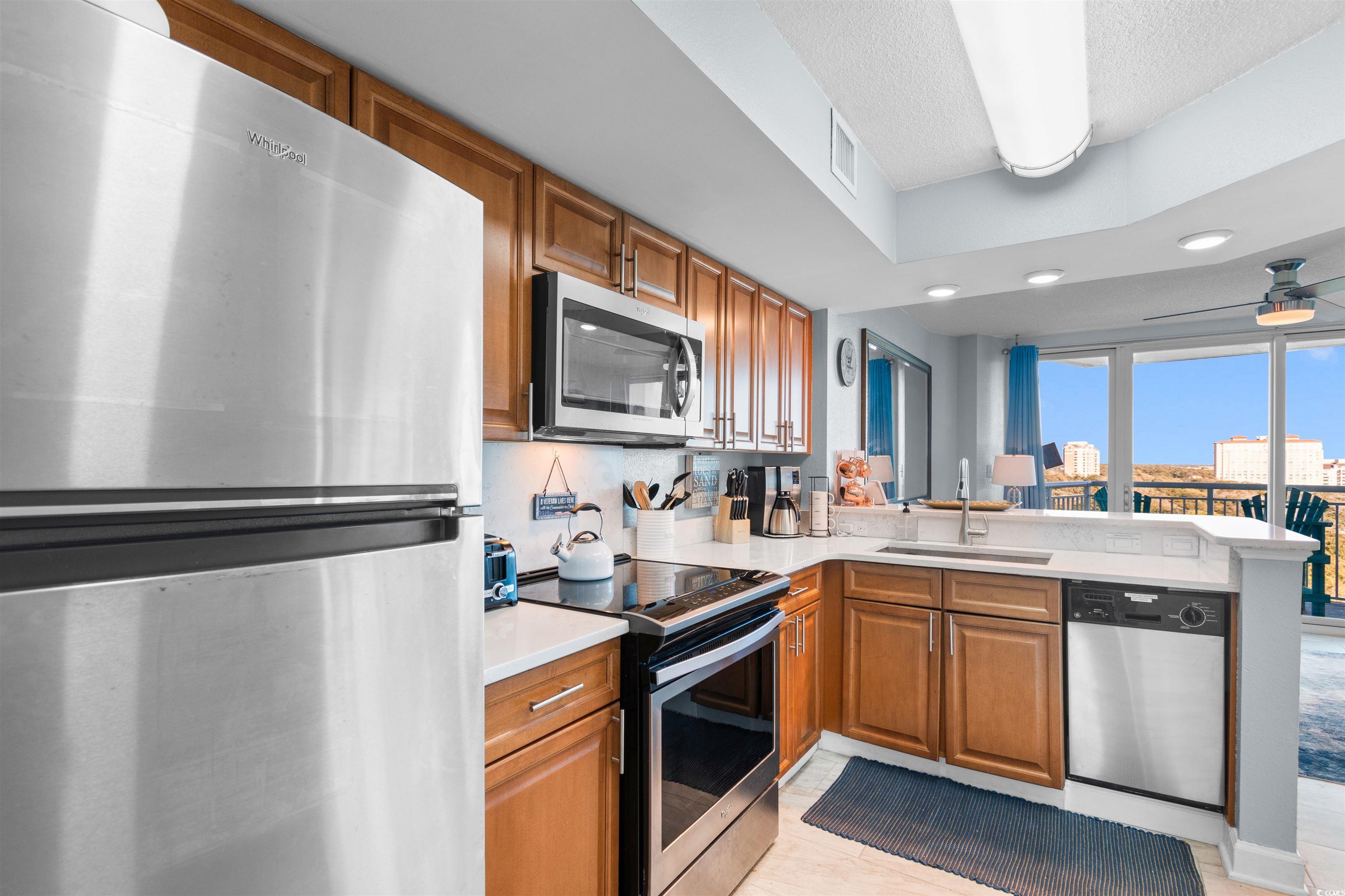 215 77th Avenue North, Unit 603 Myrtle Beach, SC 29572 - Photo 32 of 37 Kitchen with stainless steel appliances, brown cabinetry, a peninsula, ceiling fan, and light stone countertops