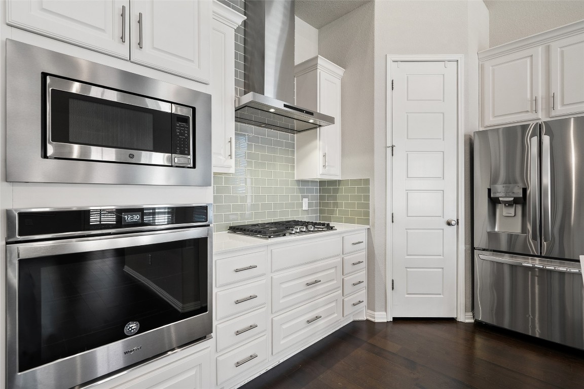 2909 Zelma Drive Cedar Park, TX 78613 - Photo 12 of 40 Kitchen featuring appliances with stainless steel finishes, wall chimney range hood, white cabinets, backsplash, and dark wood-style floors