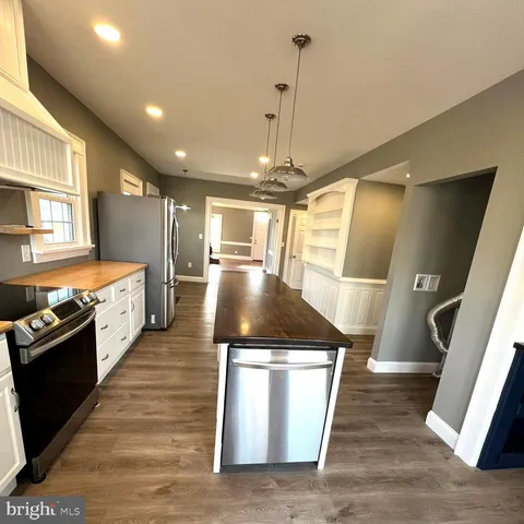 a room with stainless steel appliances kitchen island granite countertop a stove a sink and a wooden floors