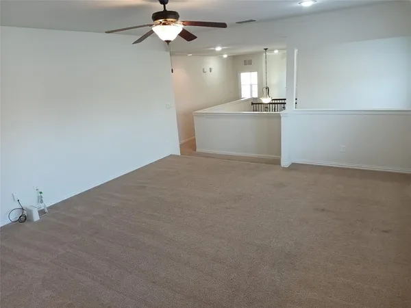 an empty room with kitchen view and a chandelier fan